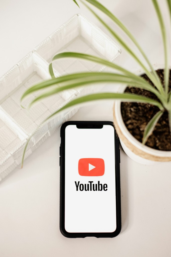 Smartphone displaying the YouTube app on a clean desk with a plant nearby