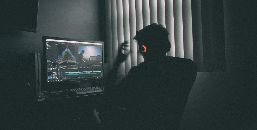 Video editor at a desk with headphones reviewing footage on a monitor in a dark studio