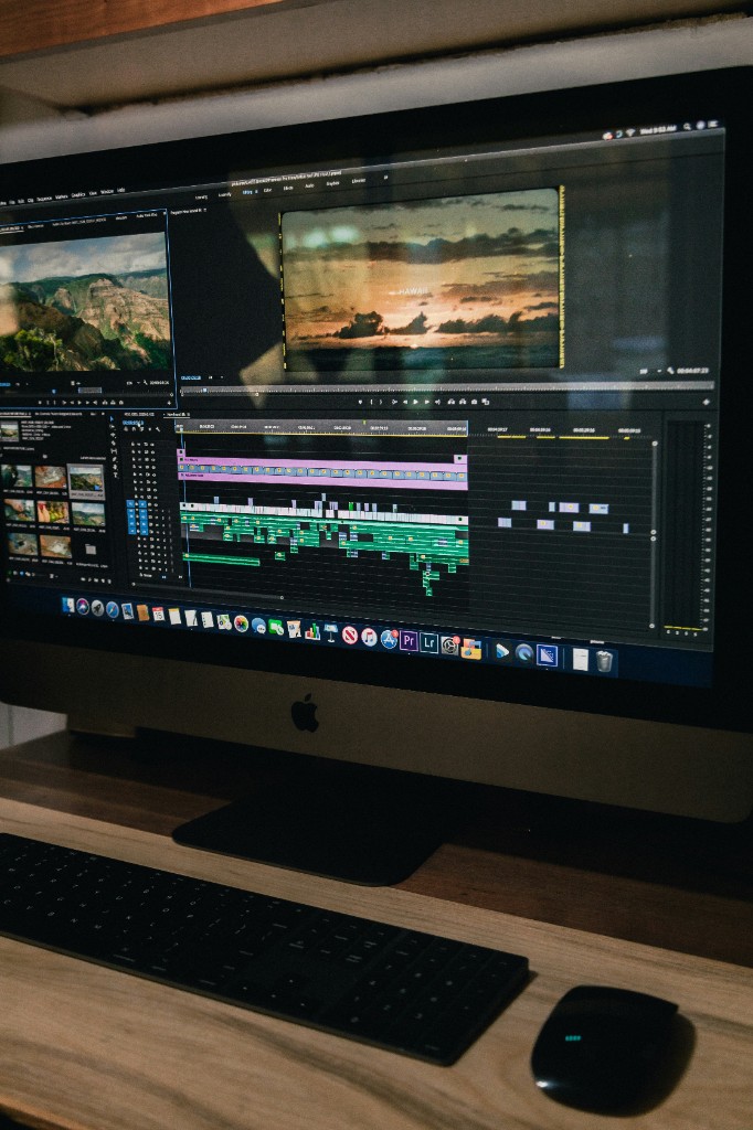 Video editor at an iMac workstation with Adobe Premiere Pro open on screen